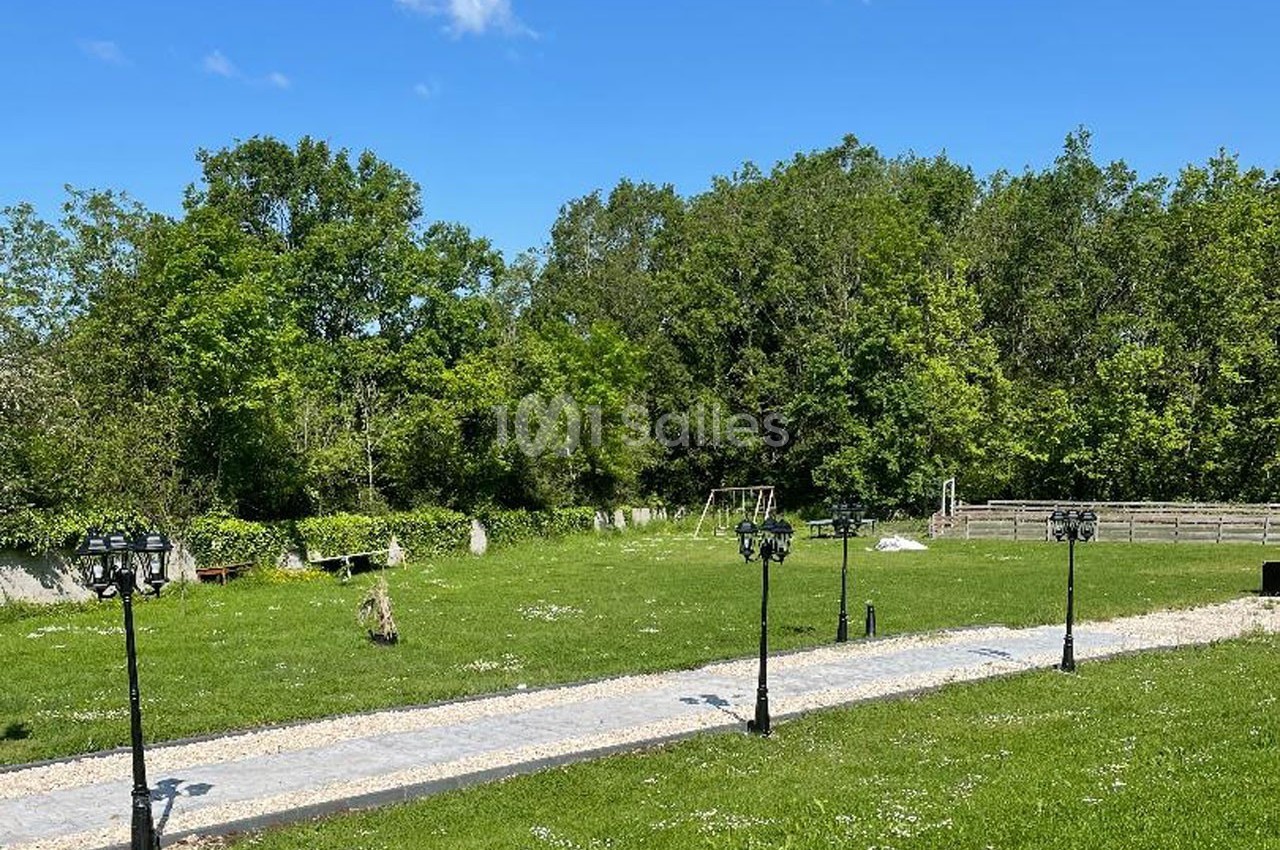 Allée pavée bordée de lampadaires dans un grand jardin verdoyant avec des arbres en arrière-plan.