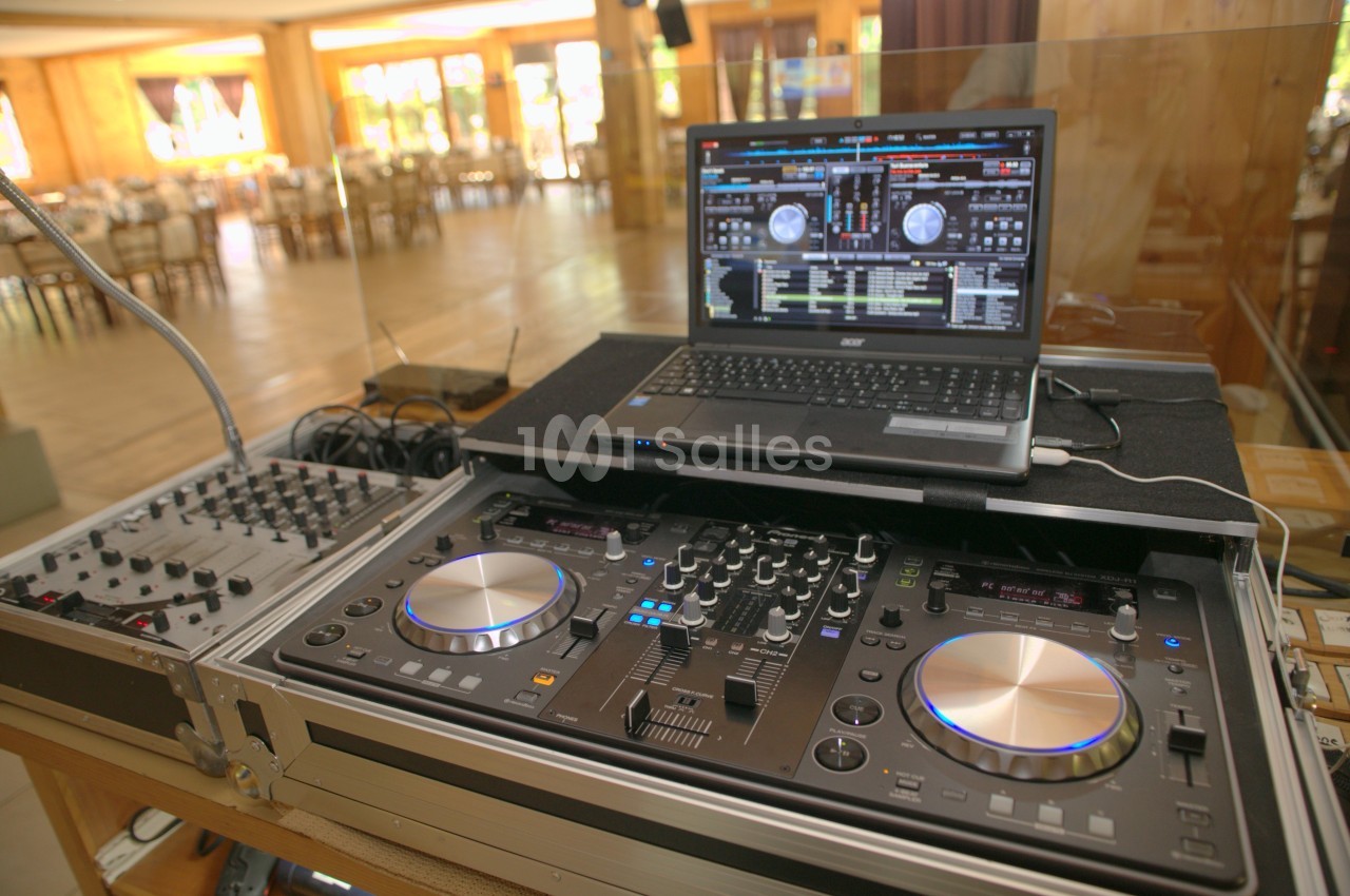 Table de mixage avec platines et ordinateur portable affichant un logiciel de DJ, installée dans une salle lumineuse.