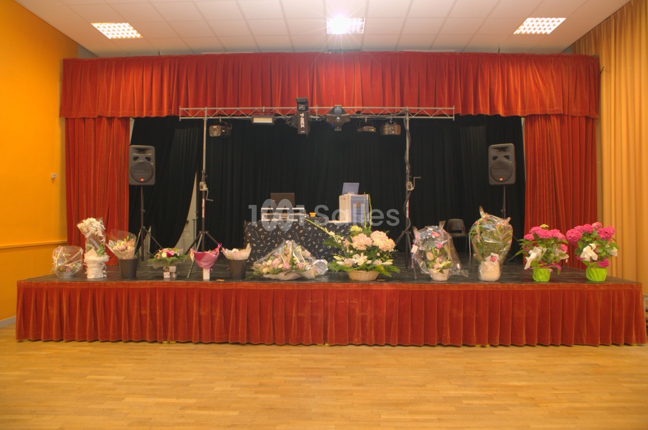 Scène décorée de fleurs avec des rideaux rouges, des équipements audio et un éclairage de salle.