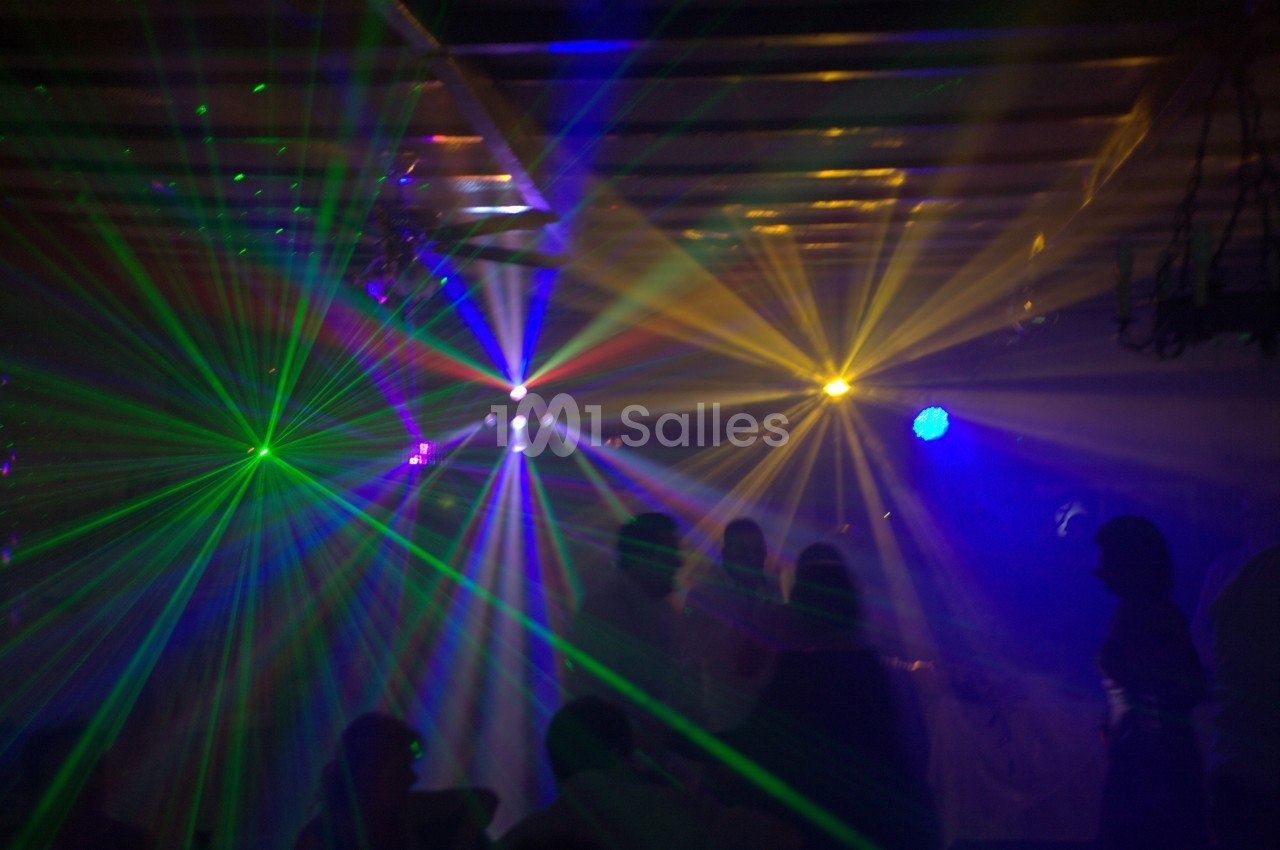 Des faisceaux lumineux colorés traversent une salle sombre remplie de silhouettes de personnes.