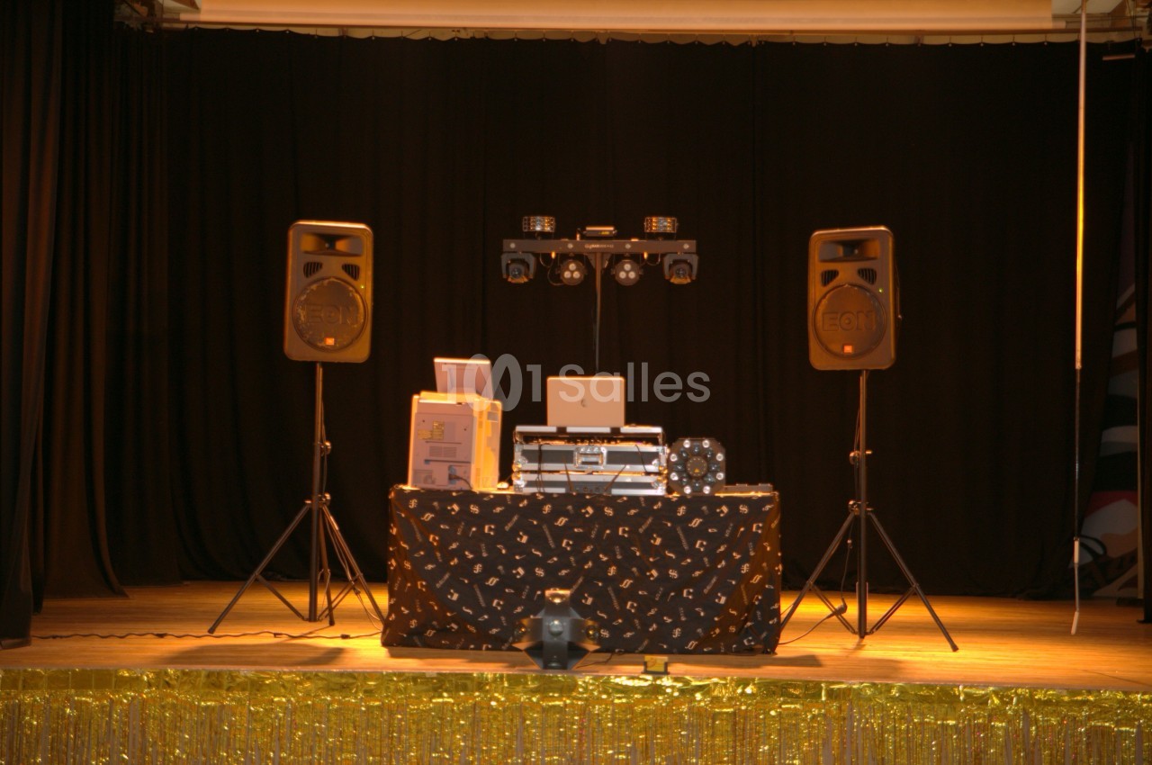 Table de DJ équipée de matériel audio et éclairage, installée sur une scène avec rideaux noirs en arrière-plan.