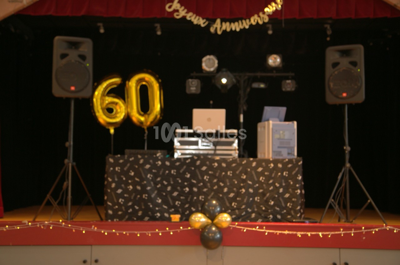 Table de DJ décorée pour un 60e anniversaire, avec ballons dorés, guirlandes lumineuses et équipements audio sur scène.