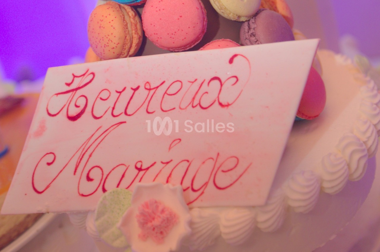 Plaque en sucre avec l'inscription ’Heureux Mariage’ posée sur un gâteau décoré de macarons colorés.