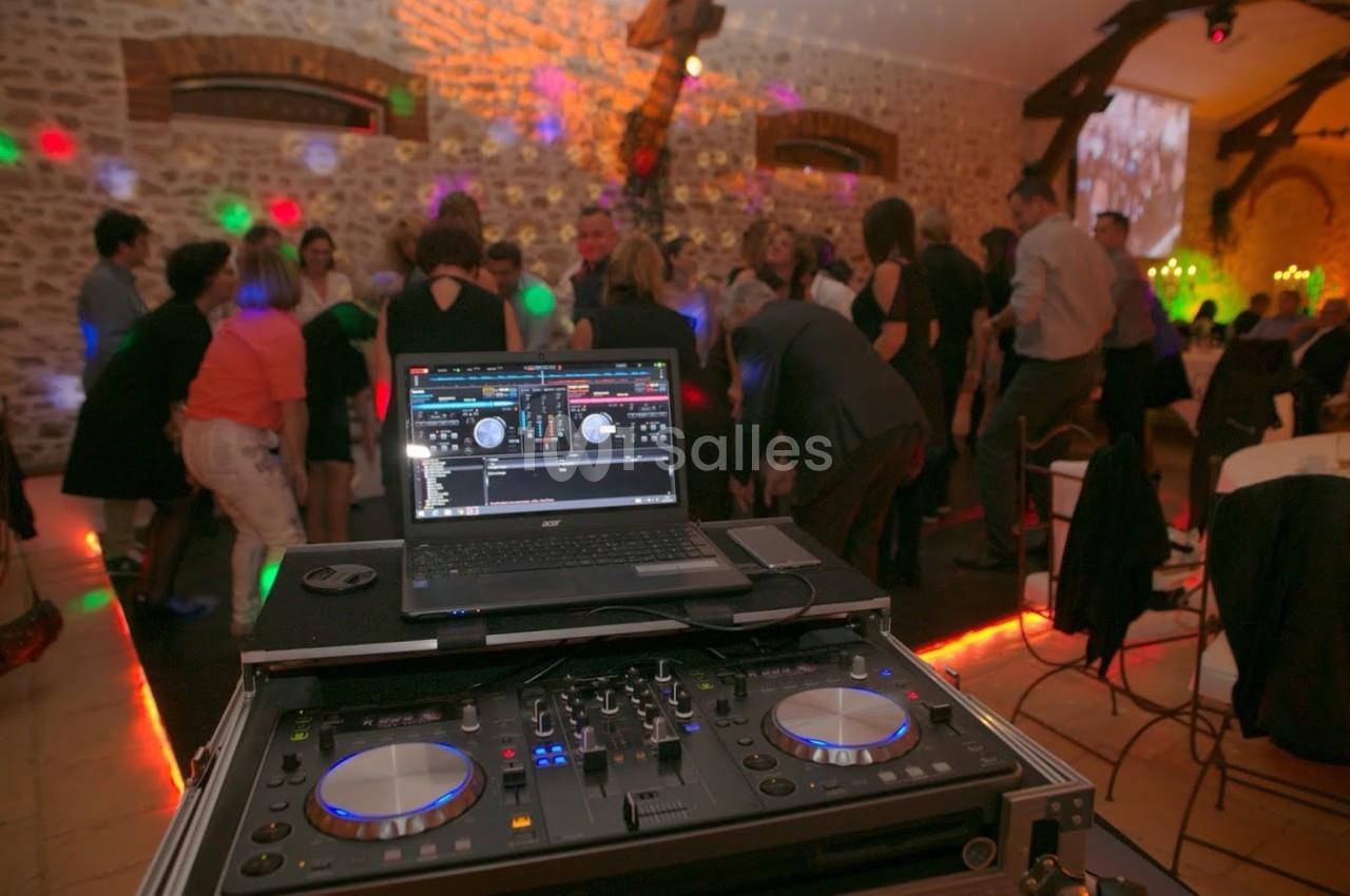 Une piste de danse animée lors d'une soirée, avec une console de DJ et un ordinateur au premier plan.