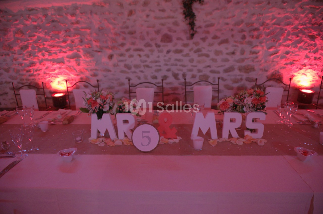 Table de mariage décorée avec des fleurs, des lettres ’MR & MRS’ et un chiffre 5, éclairée par une lumière rose.