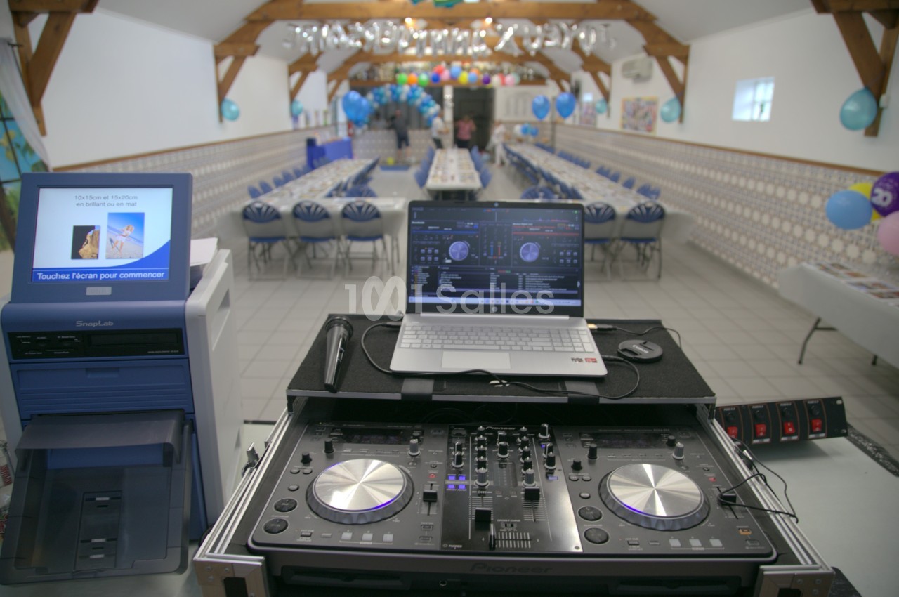 Table de mixage et ordinateur installés dans une salle décorée pour un événement, avec tables et ballons en arrière-plan.