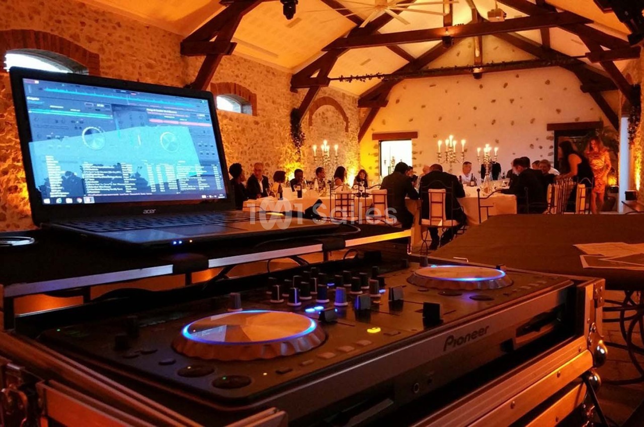 Console de DJ en gros plan dans une salle de réception éclairée, avec des invités attablés en arrière-plan.