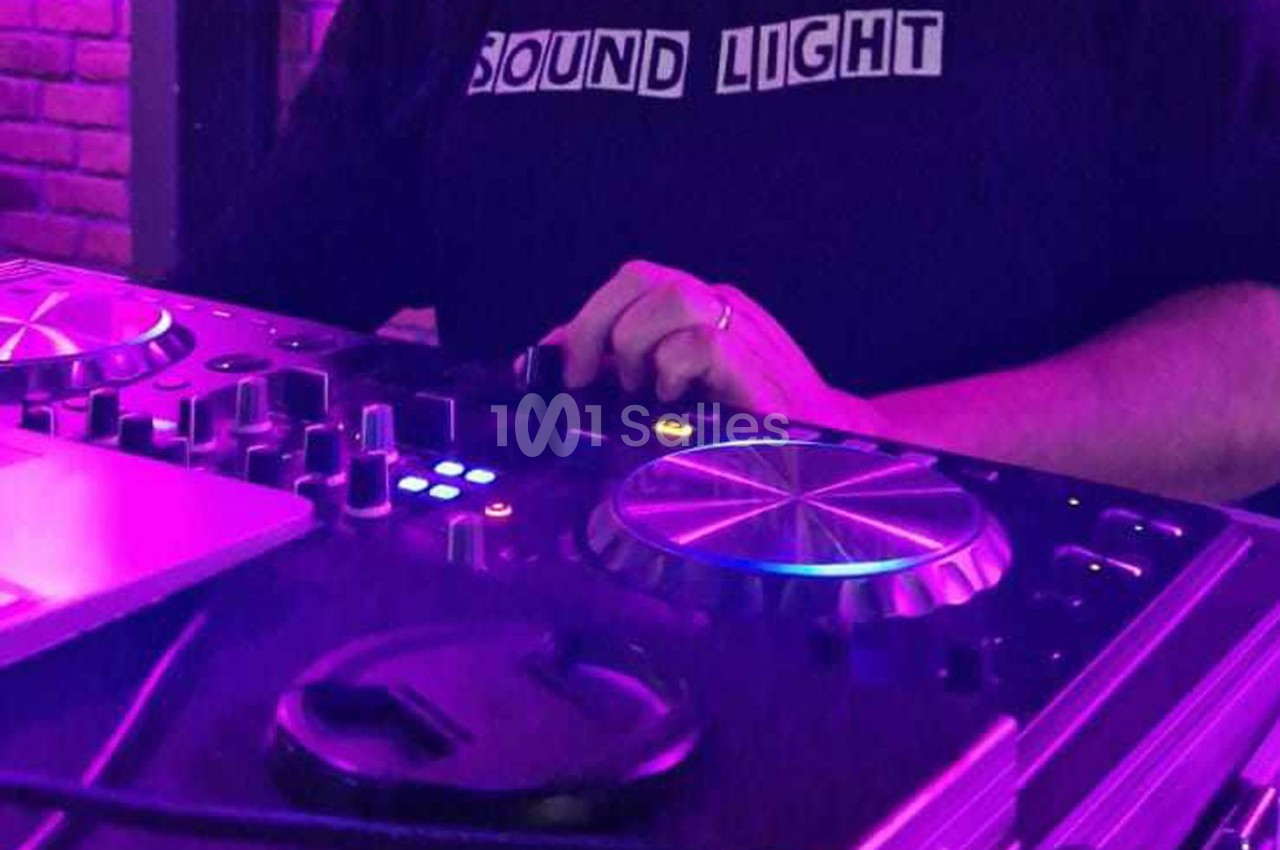 Personne ajustant les commandes d'une table de mixage DJ sous un éclairage violet.