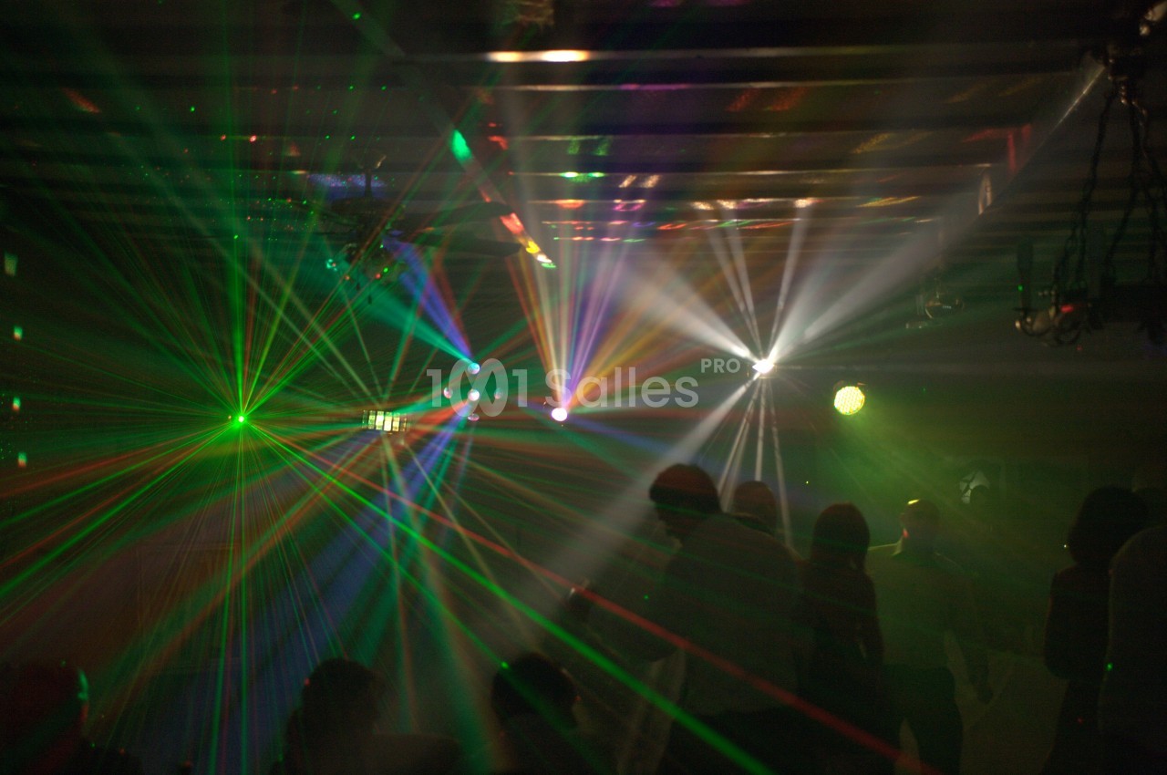 Jeux de lumières colorées et faisceaux laser éclairant une salle sombre avec des silhouettes de personnes.
