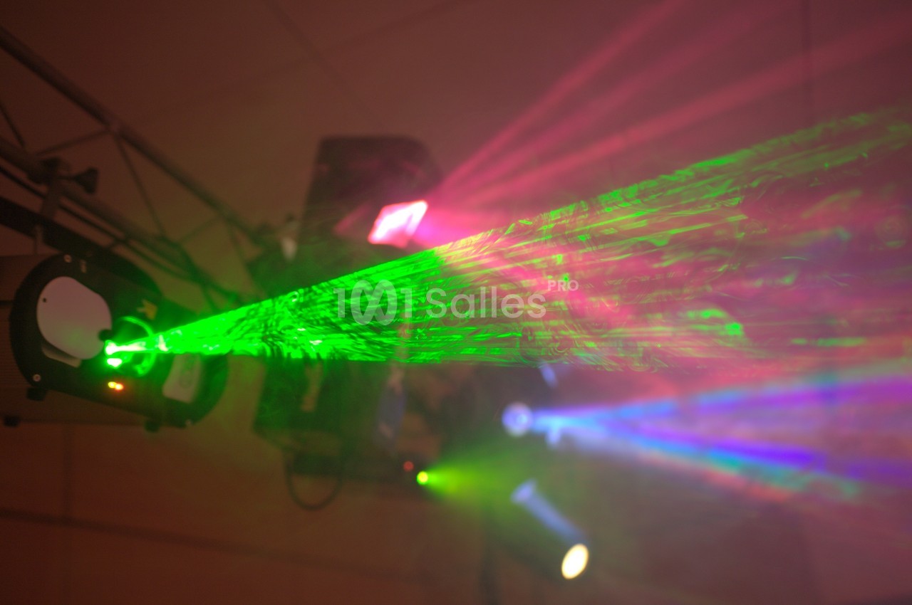 Faisceau laser vert projeté dans une ambiance sombre avec des lumières colorées en arrière-plan.