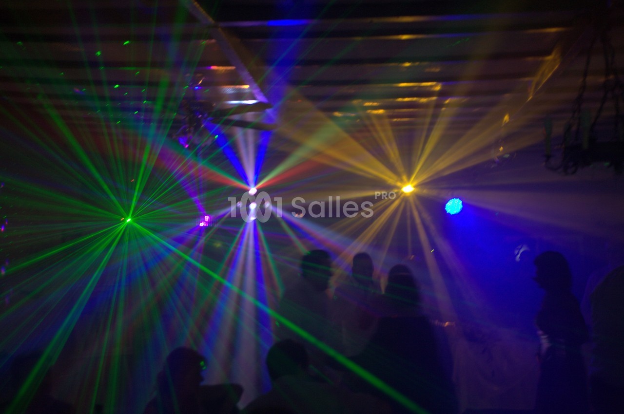 Des faisceaux lumineux colorés traversent une salle sombre remplie de silhouettes de personnes.