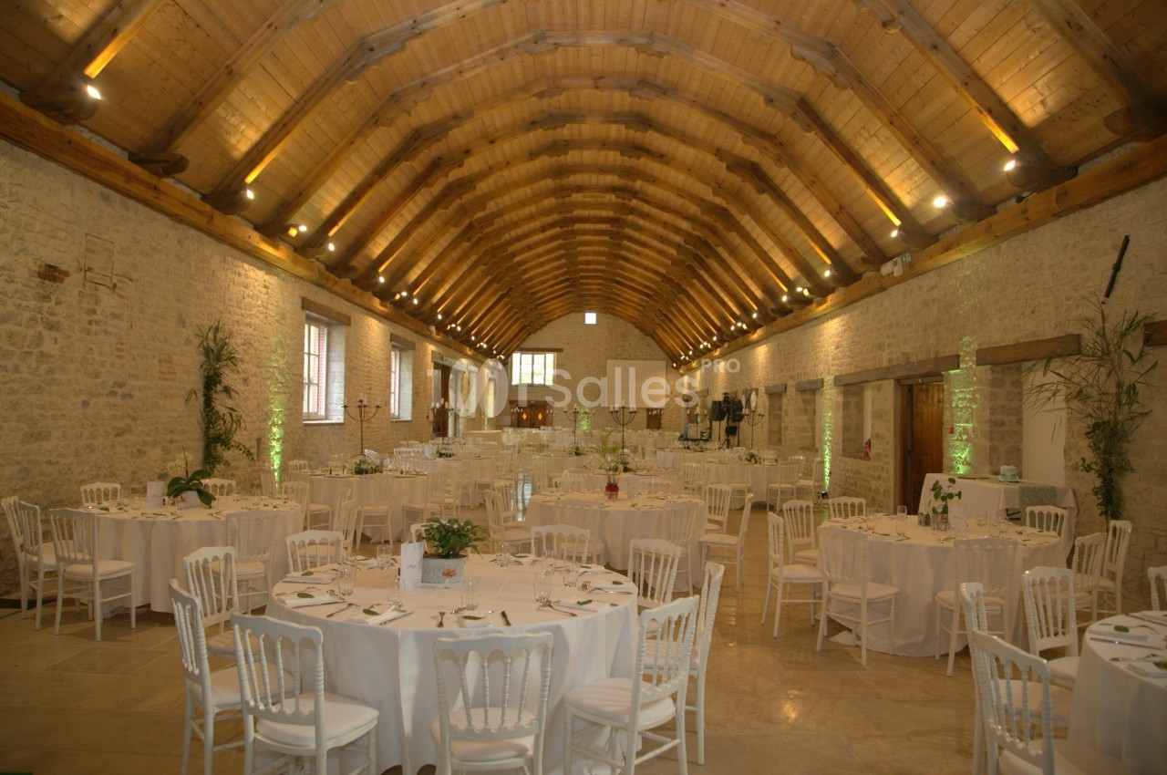 Salle de réception en pierre avec plafond voûté en bois, tables rondes dressées et éclairage chaleureux.
