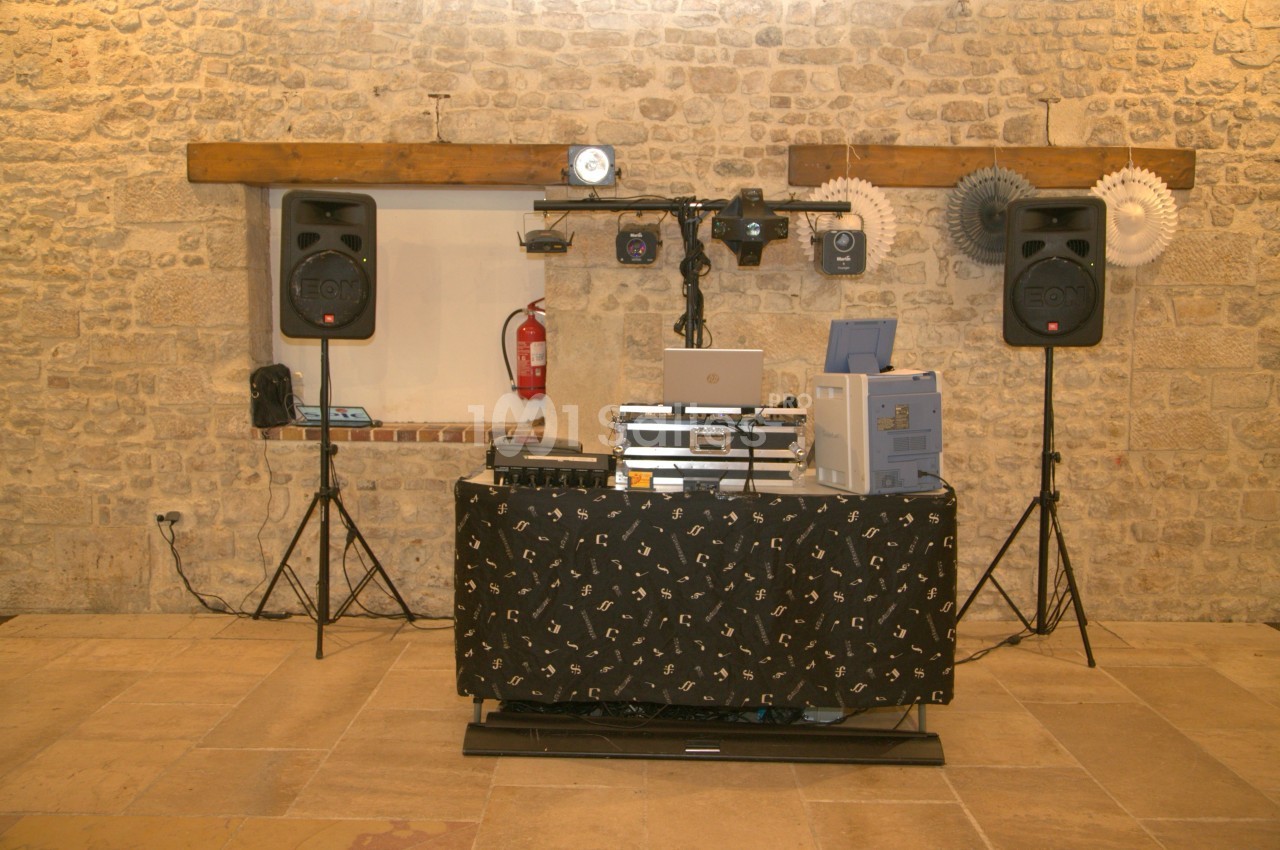 Installation de matériel de sonorisation et d'éclairage dans une salle en pierre avec une table recouverte d'un tissu noir.