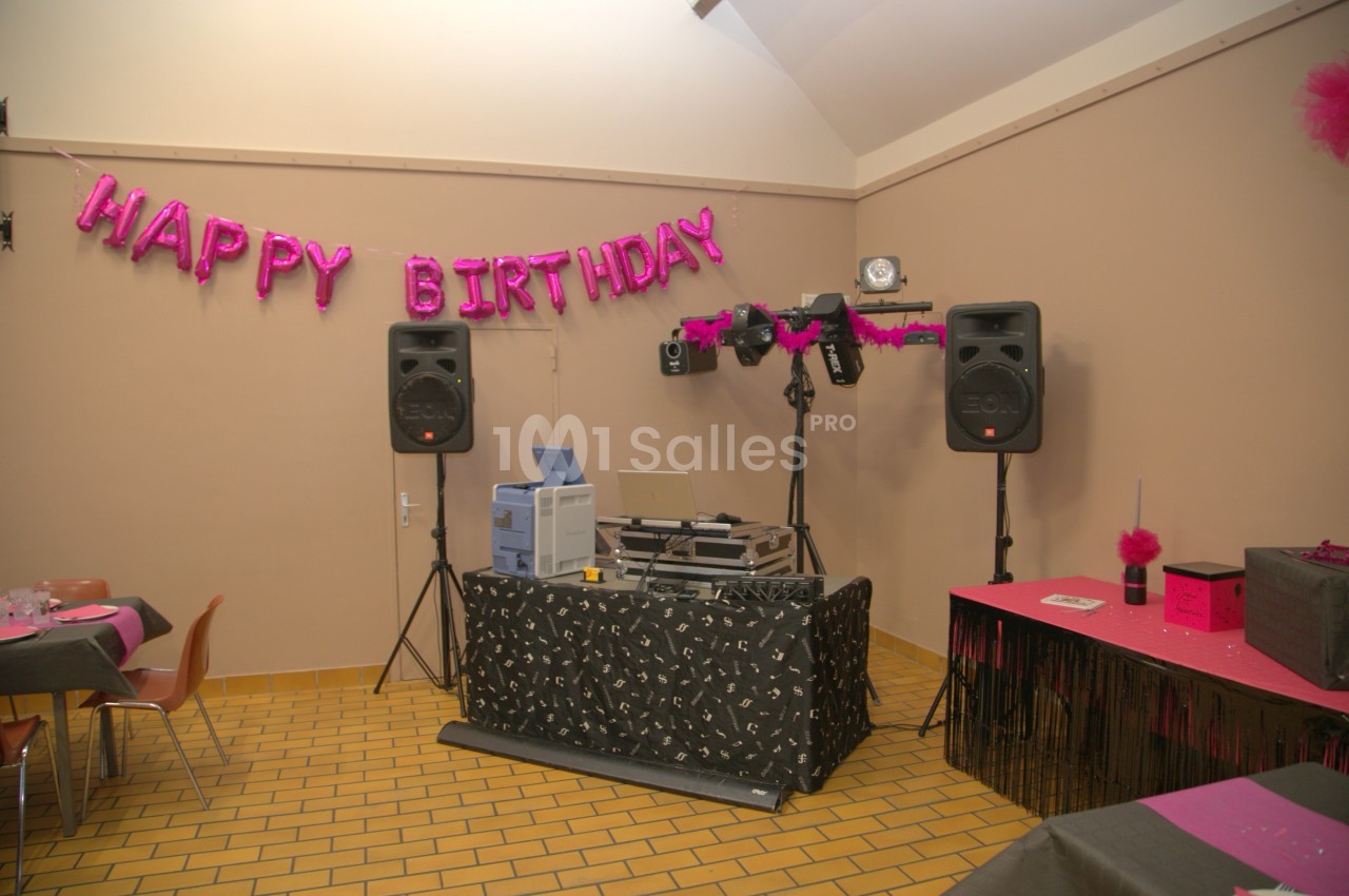 Salle décorée pour un anniversaire avec une table de mixage, des enceintes et une bannière ’Happy Birthday’.