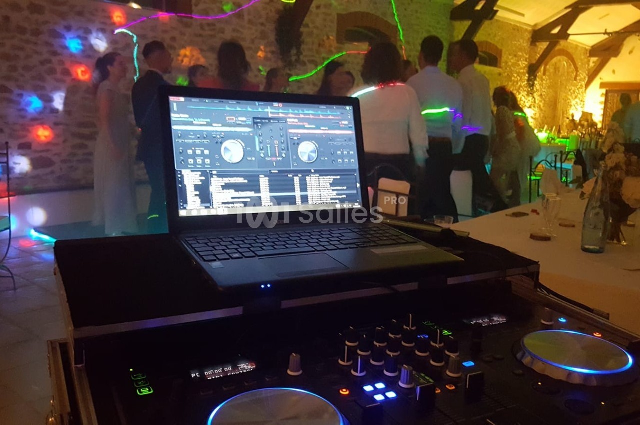 Ordinateur portable avec logiciel de mixage sur une table de DJ, devant une piste de danse éclairée par des lumières…