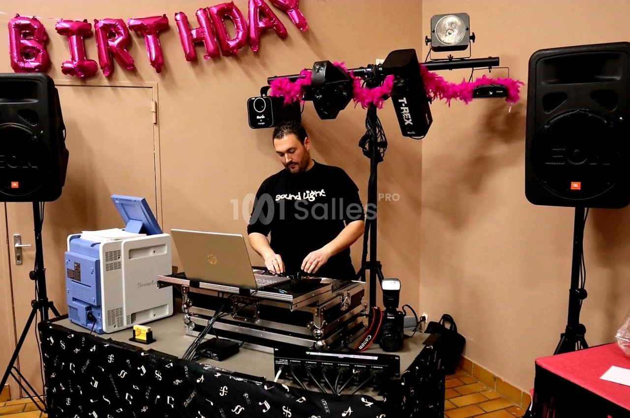Un DJ mixant de la musique sur une table équipée d'un ordinateur et de matériel audio lors d'une fête d'anniversaire.