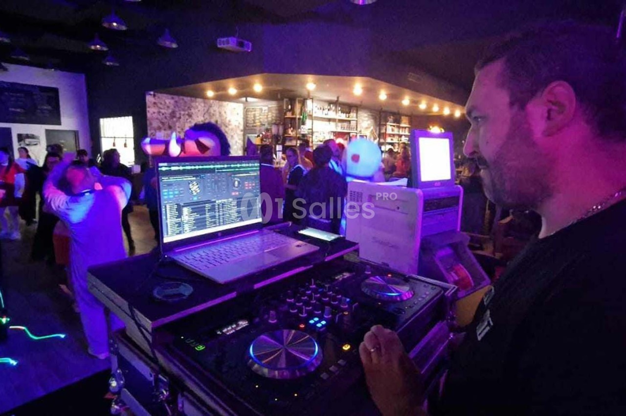 Un DJ mixe de la musique dans un bar animé avec des lumières colorées et des danseurs en arrière-plan.