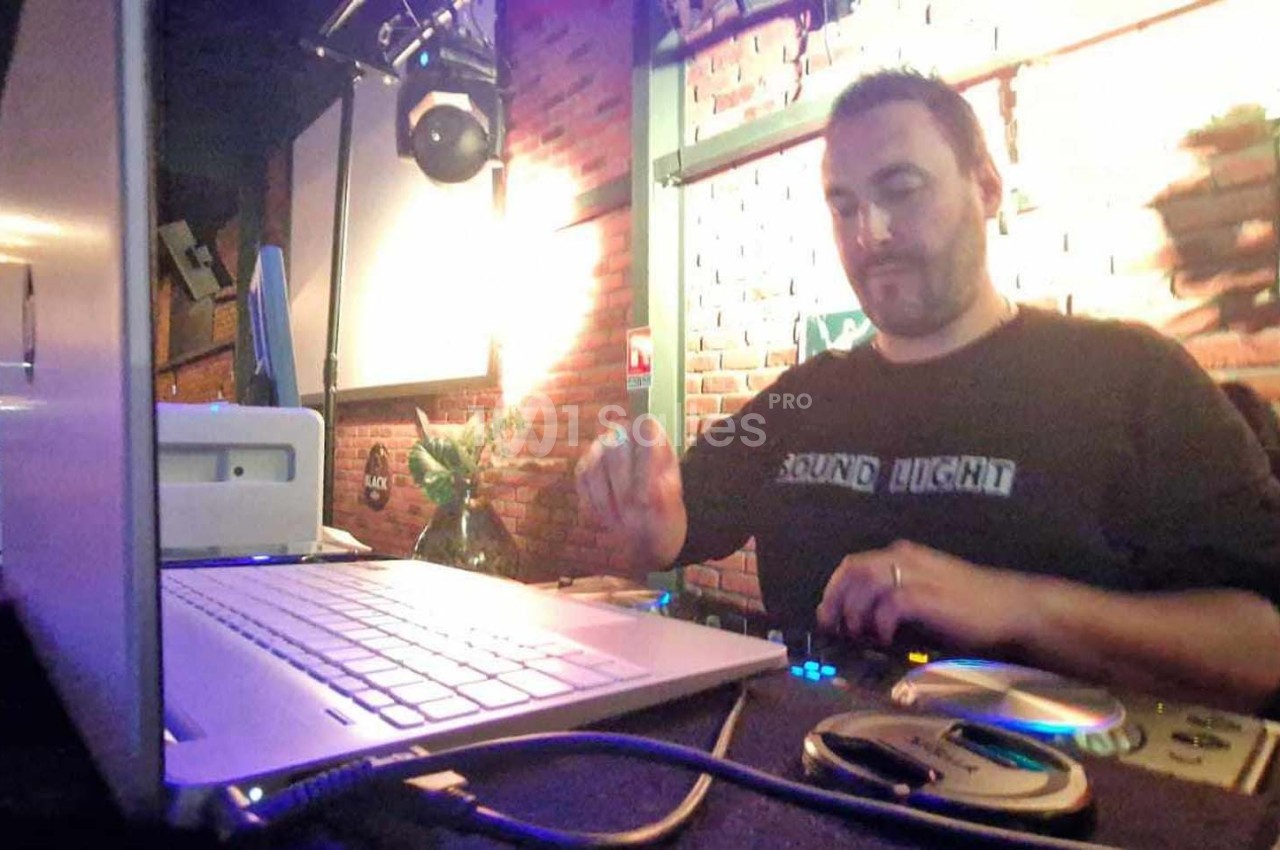 Un DJ mixe de la musique sur une console dans un bar à l'ambiance tamisée avec des lumières chaudes.