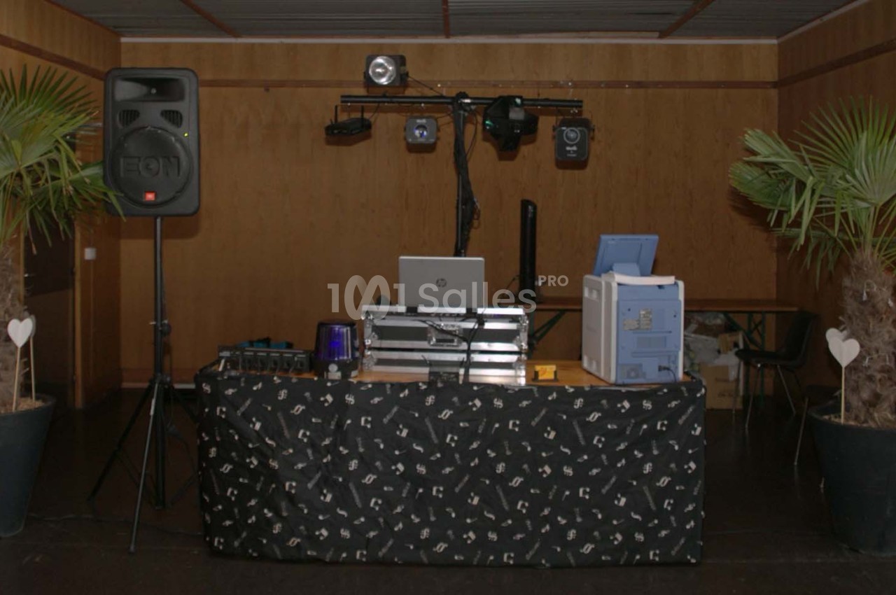 Table de mixage avec équipement audio et éclairage, encadrée par deux plantes en pot, dans une salle au mur en bois.