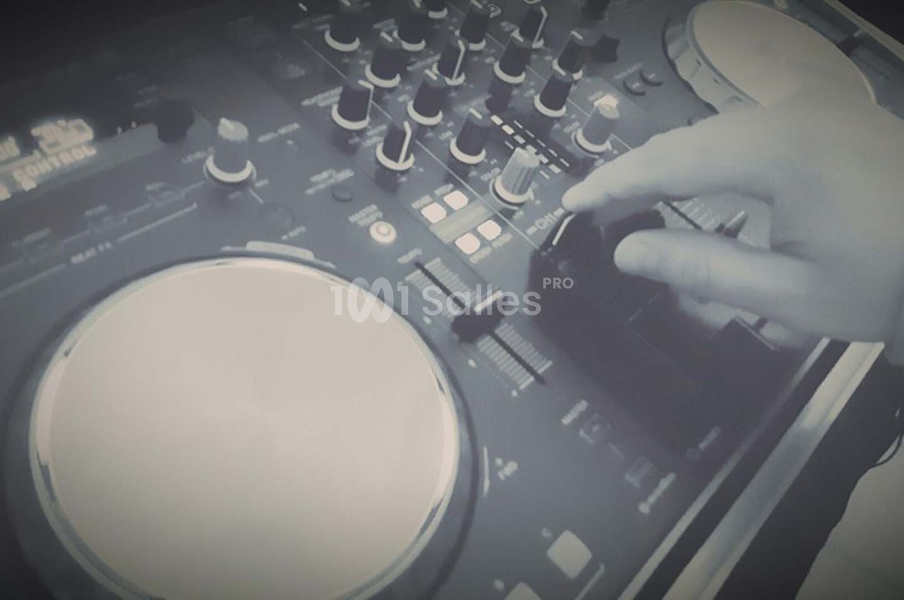 Main ajustant un bouton sur une table de mixage DJ avec des platines et des commandes visibles.