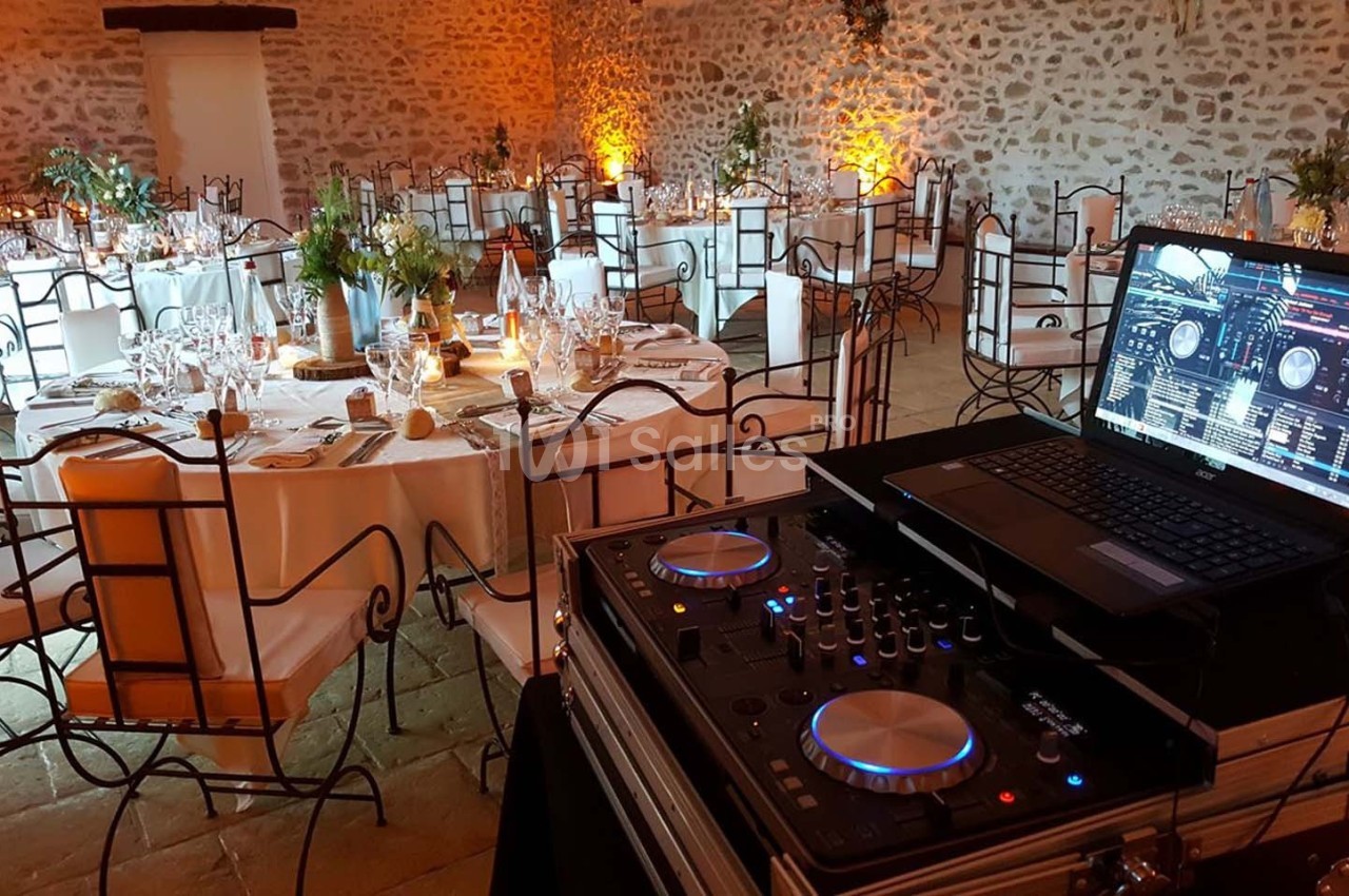 Salle de réception décorée avec des tables dressées et un poste de DJ équipé d'un ordinateur portable au premier plan.