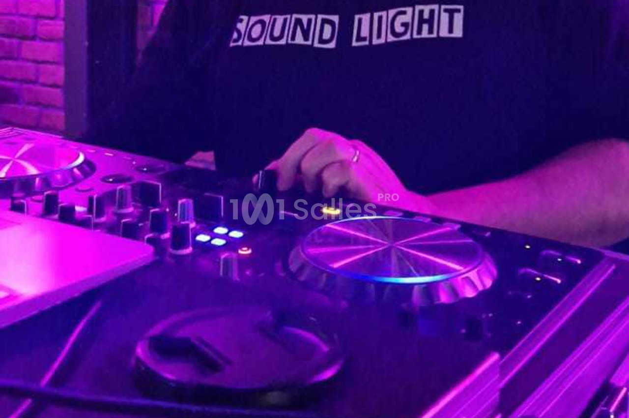 Personne ajustant les commandes d'une table de mixage DJ sous un éclairage violet.