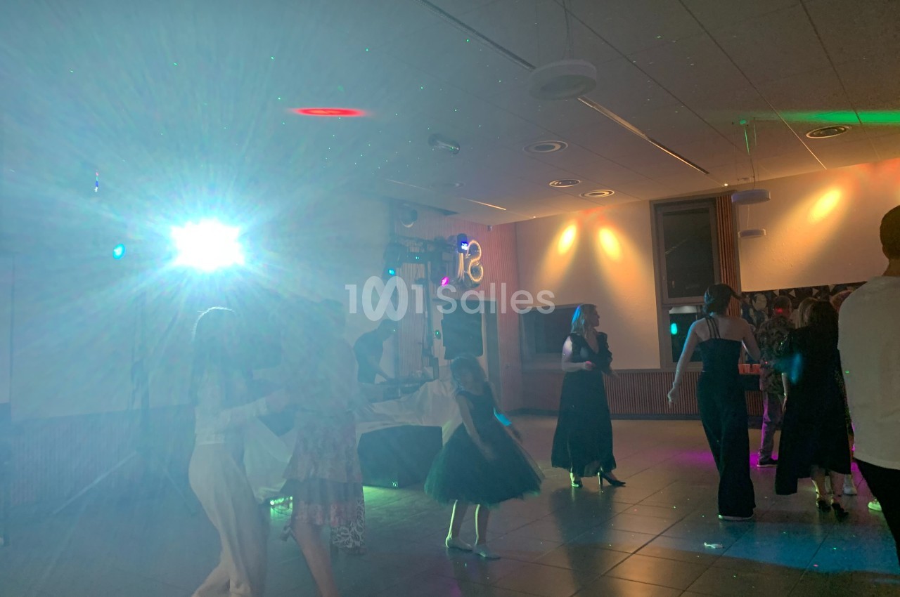 Des personnes dansent dans une salle éclairée par des lumières colorées et un projecteur.
