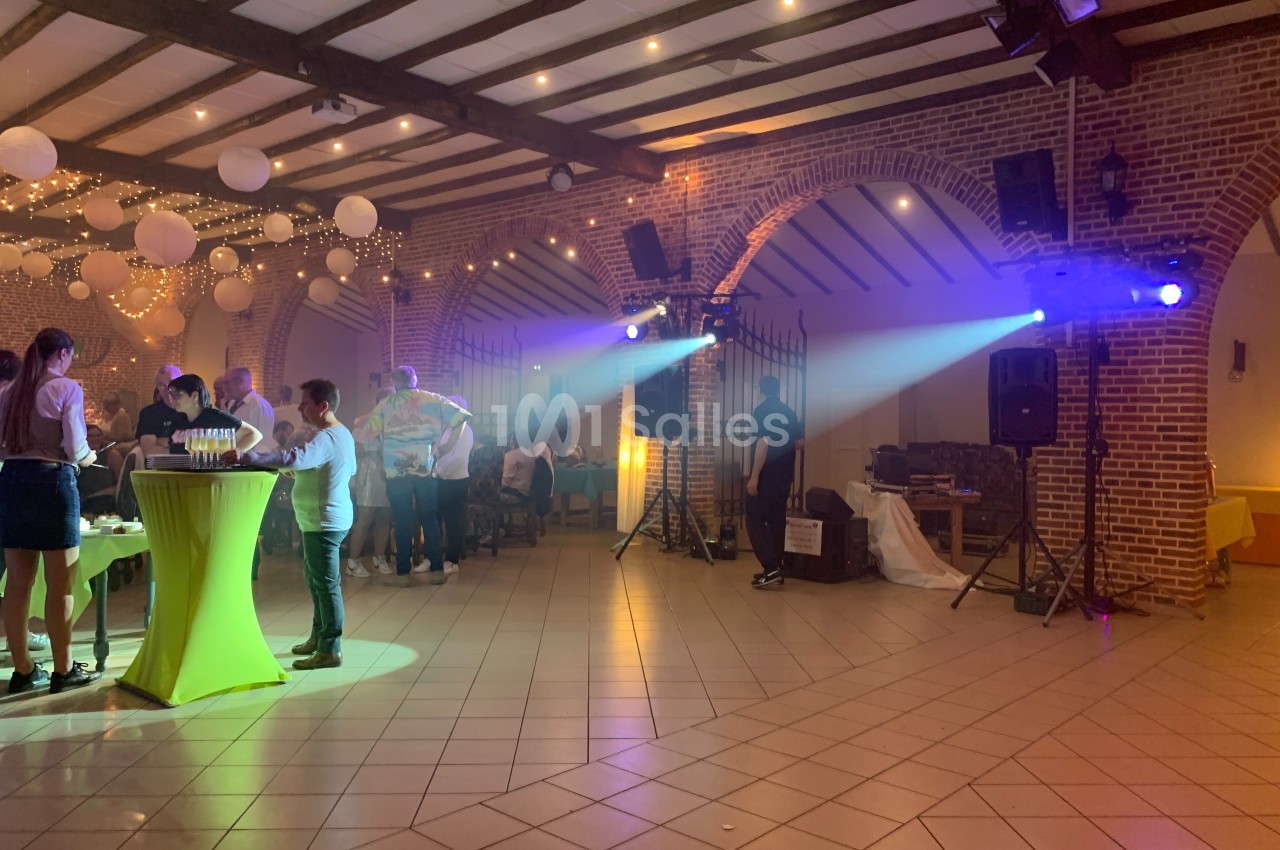 Salle de réception avec invités debout près de tables, éclairage coloré et décorations suspendues.