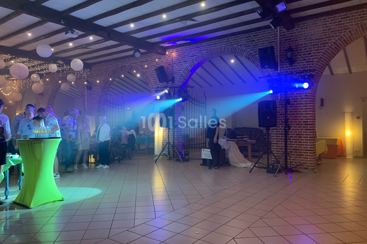 Salle de réception avec invités debout et assis, éclairages colorés et décorations suspendues.