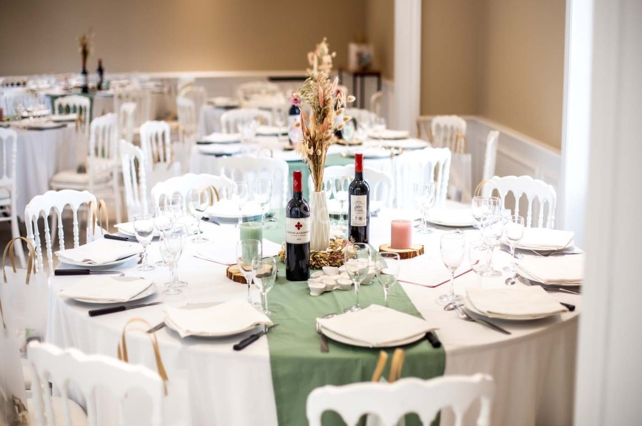 Tables élégamment dressées avec nappes blanches, chemins de table verts, bouteilles de vin et décorations florales.