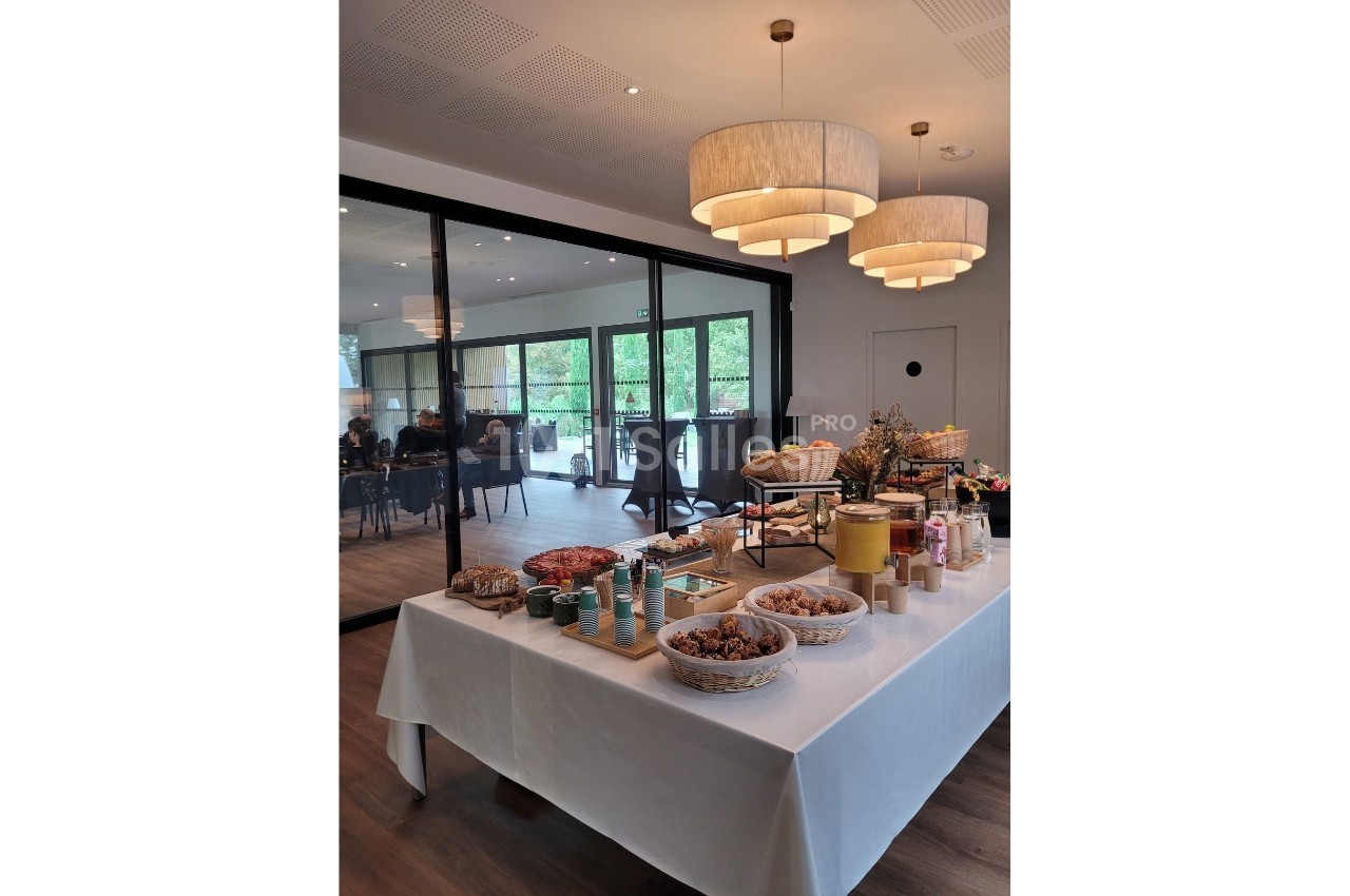 Table dressée avec des produits alimentaires variés, dans une salle lumineuse avec des personnes en arrière-plan.