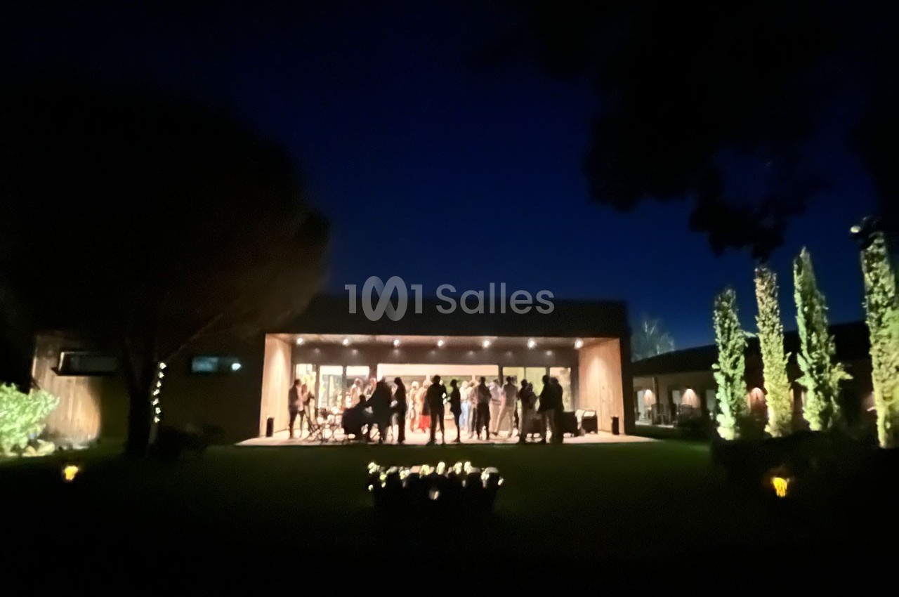 Groupe de personnes rassemblées sur une terrasse éclairée, entourée de végétation, en soirée.