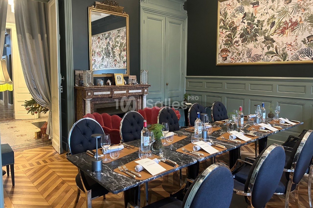 Salle à manger élégante avec une grande table dressée, chaises noires, cheminée en marbre et décor mural floral.