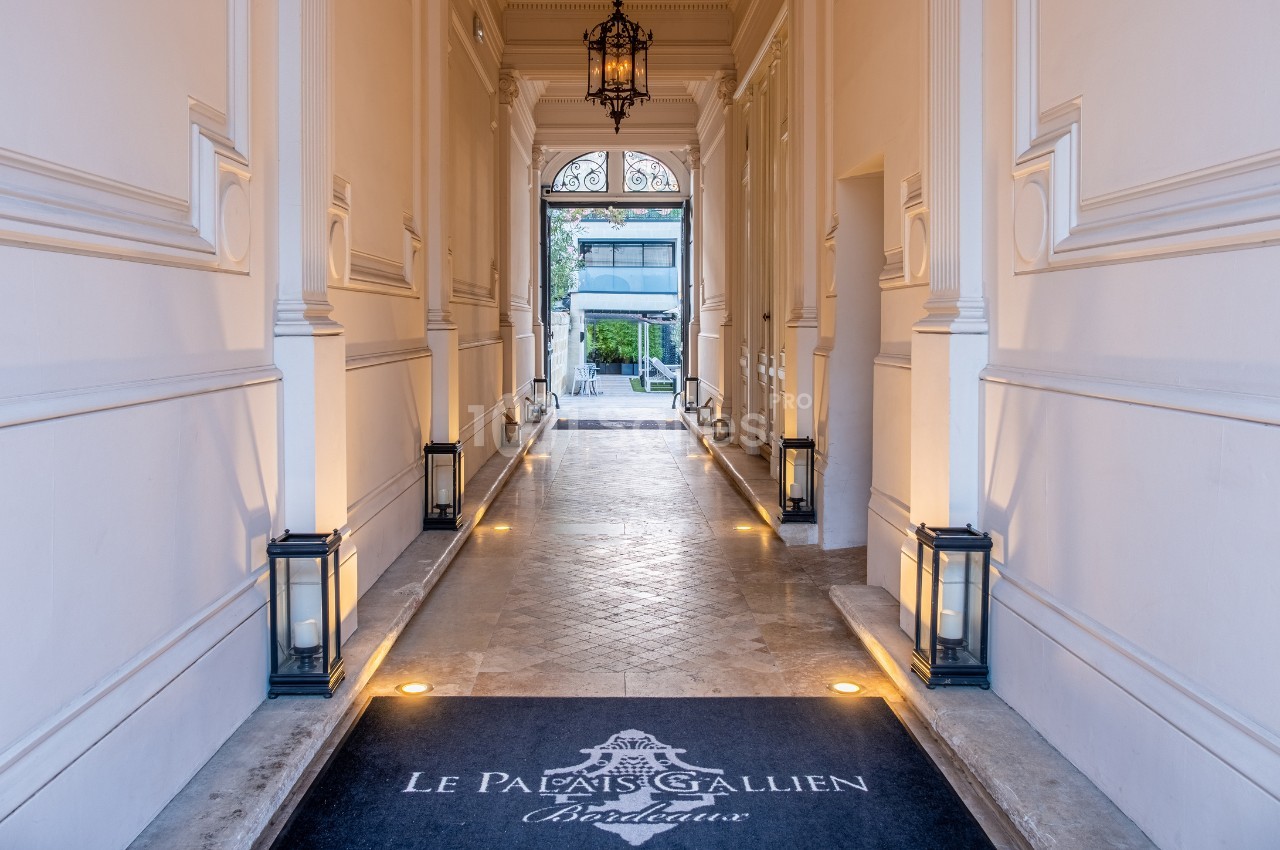 Entrée élégante d'un bâtiment avec sol en pierre, lanternes alignées et tapis marqué ’Le Palais Gallien Bordeaux’.