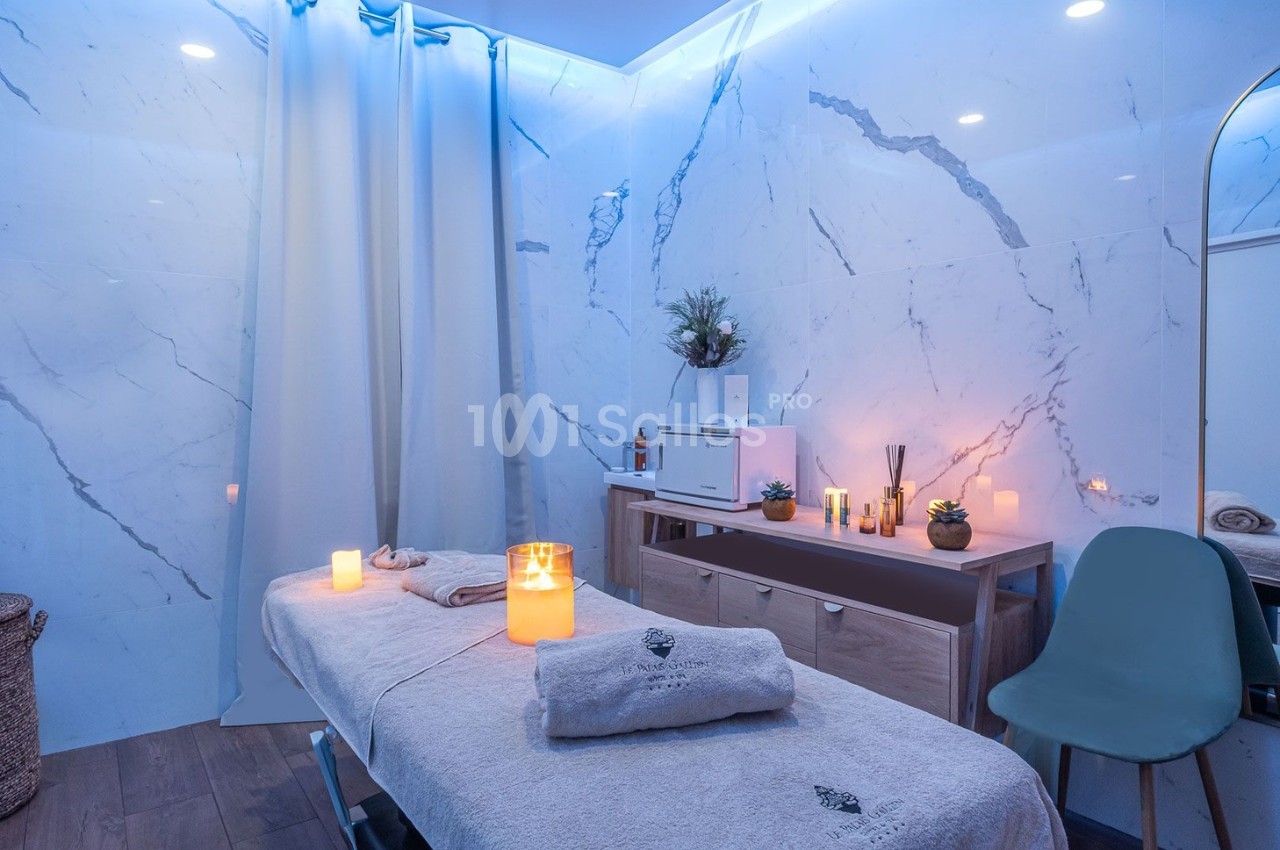 Salle de massage avec table recouverte de serviettes, éclairage tamisé et bougies pour une ambiance relaxante.