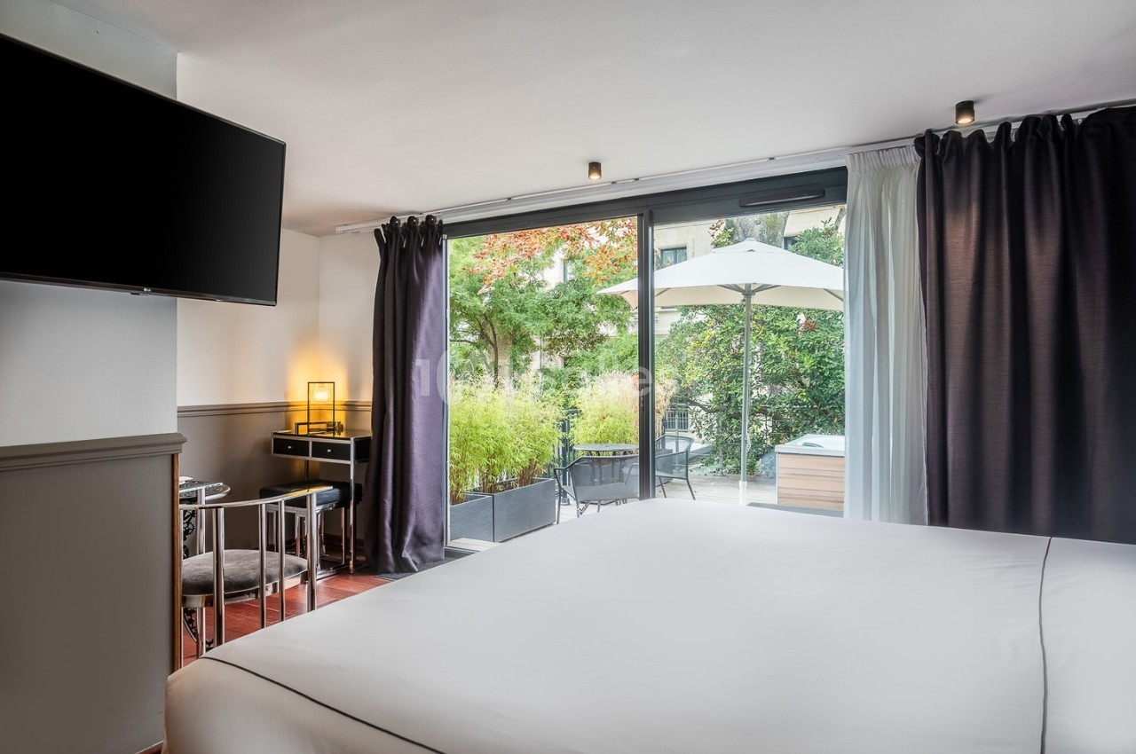 Chambre lumineuse avec lit double, bureau, télévision et accès à une terrasse avec jardin et mobilier extérieur.