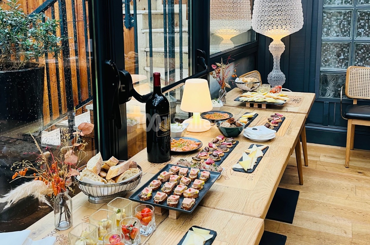 Table en bois garnie de plats variés, verrines, pains et bouteilles de vin, dans un espace lumineux avec une décoration…