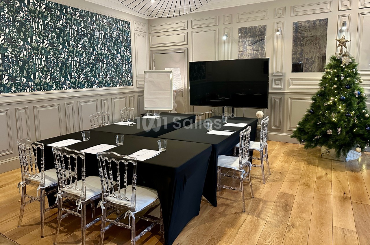 Salle de réunion décorée avec un sapin de Noël, des tables noires disposées en U et un écran plat.