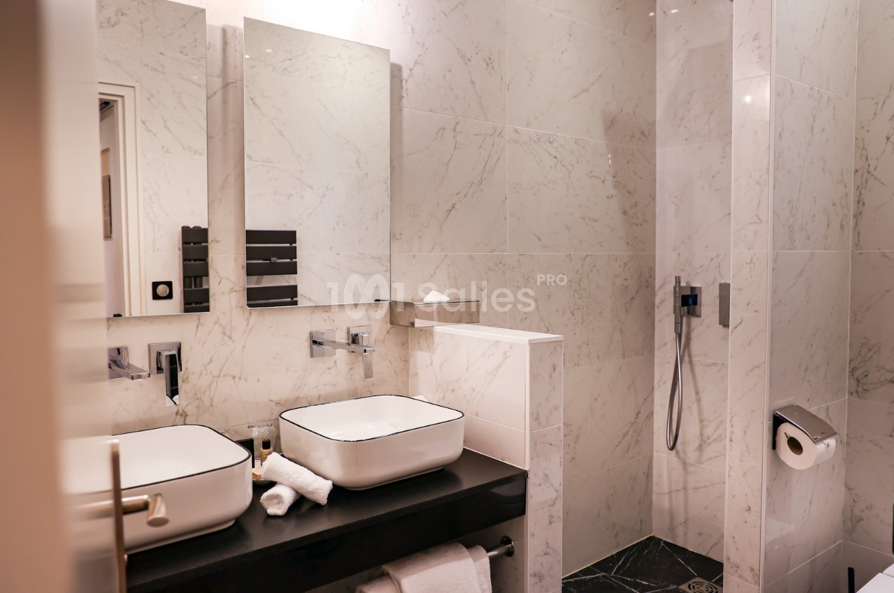 Salle de bain moderne avec deux vasques, murs en marbre clair, douche à l'italienne et accessoires minimalistes.