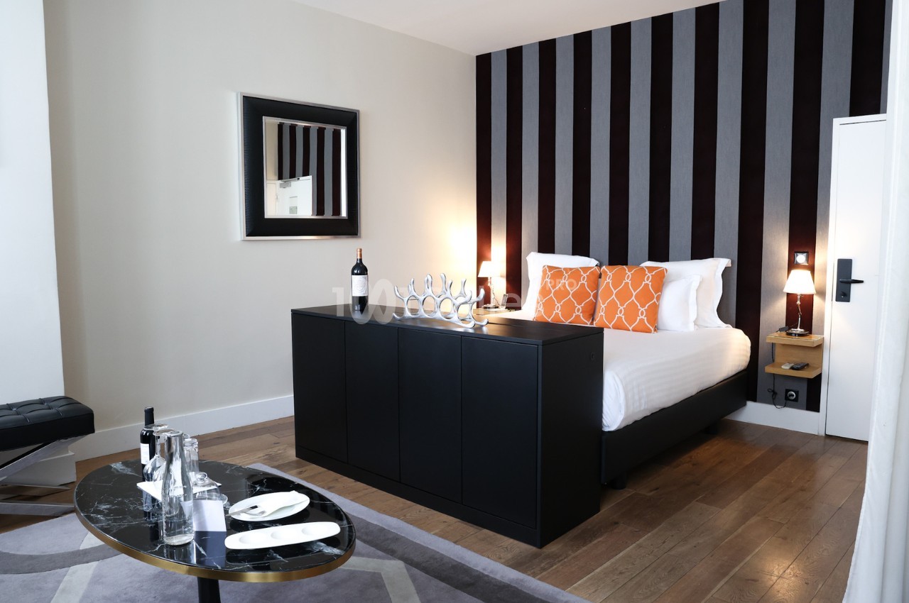 Chambre moderne avec lit double, décoration épurée, murs rayés, table basse avec plateau et bouteille de vin sur meuble.