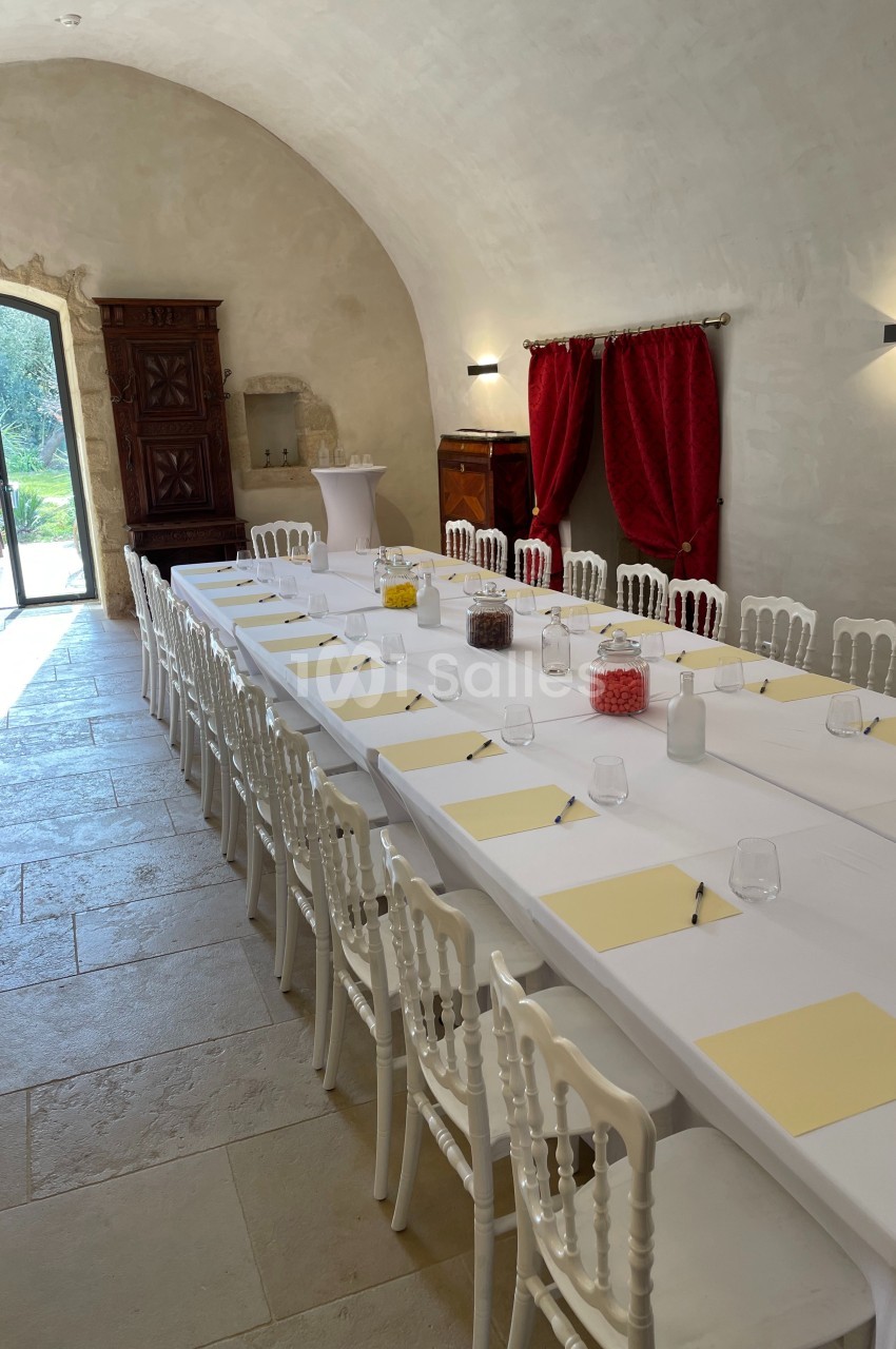 Salle voûtée aménagée pour une réunion, avec une longue table dressée de blocs-notes, verres et chaises blanches.