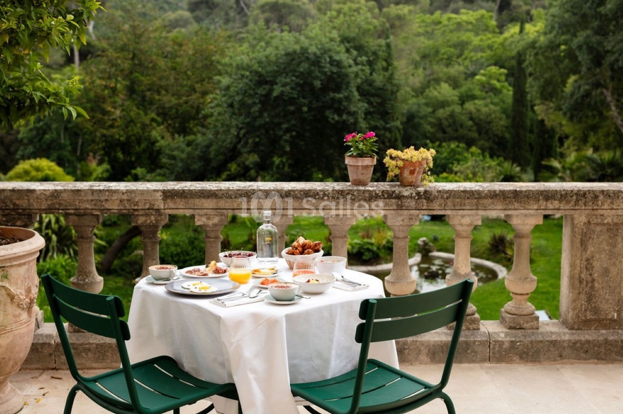 Table dressée pour un repas en plein air sur une terrasse avec vue sur un jardin verdoyant.