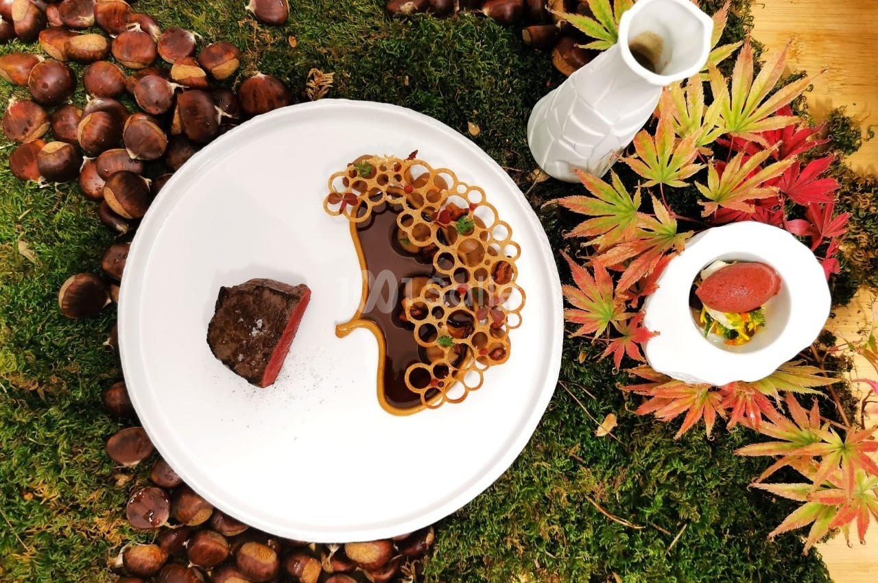 Assiette gastronomique avec viande, sauce, décorations croustillantes, présentée sur mousse, châtaignes et feuilles d…