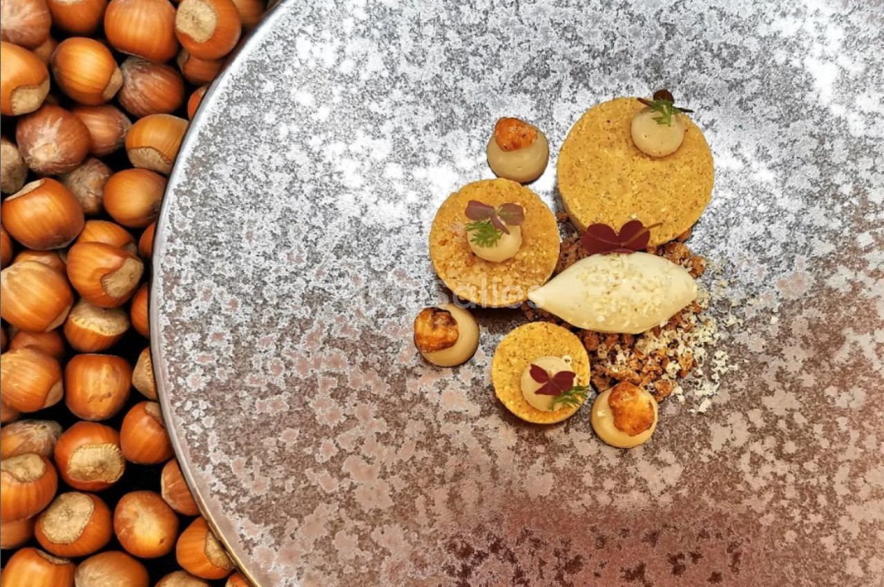 Assiette gastronomique composée de desserts aux noisettes, présentée sur un fond texturé et entourée de noisettes entières.