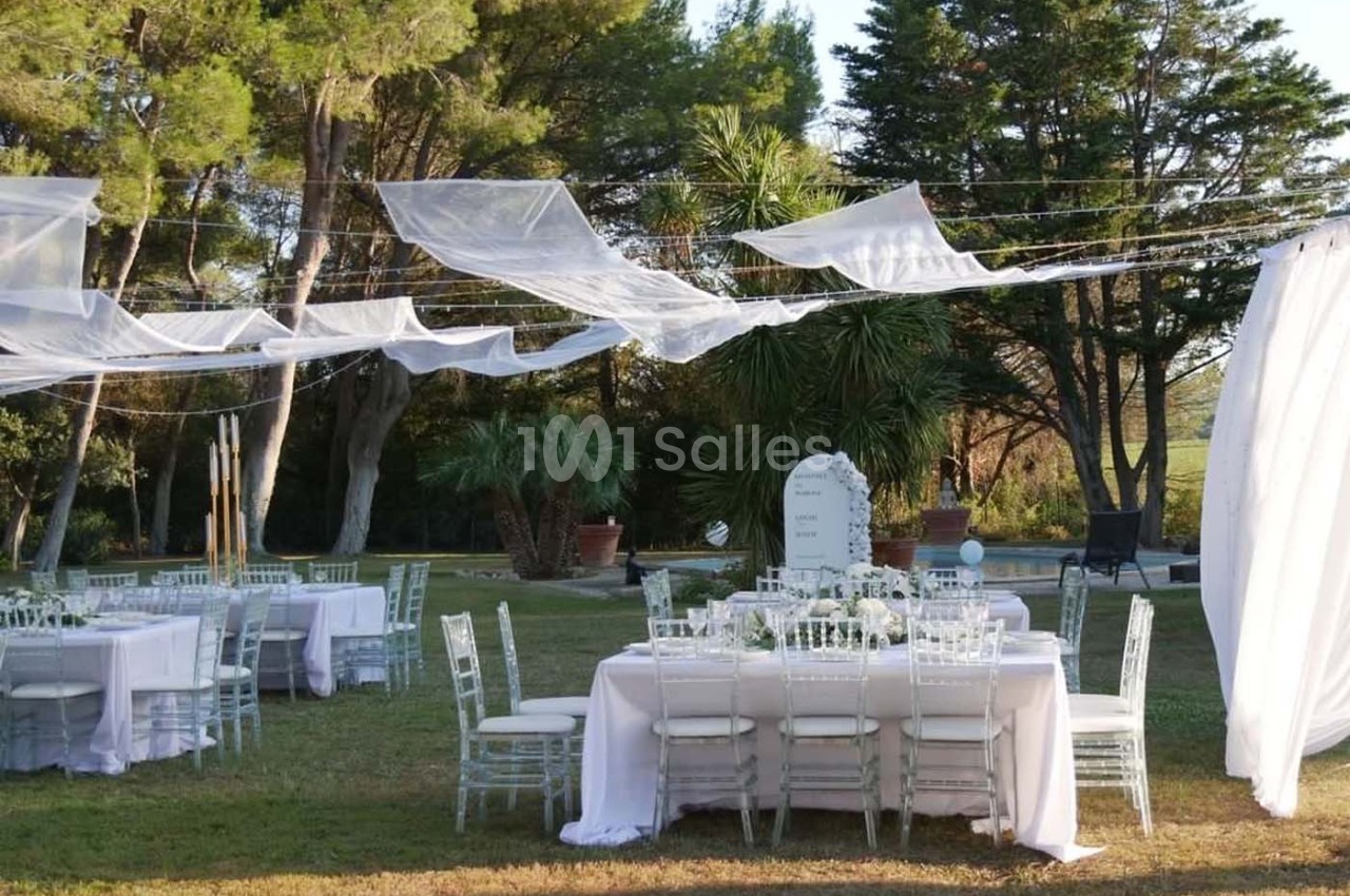 Tables décorées pour un événement en plein air, entourées de verdure et recouvertes de voiles blancs suspendus.