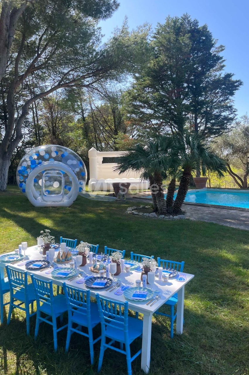 Table dressée avec des chaises bleues dans un jardin près d'une piscine, décorée pour une fête avec des ballons et un…