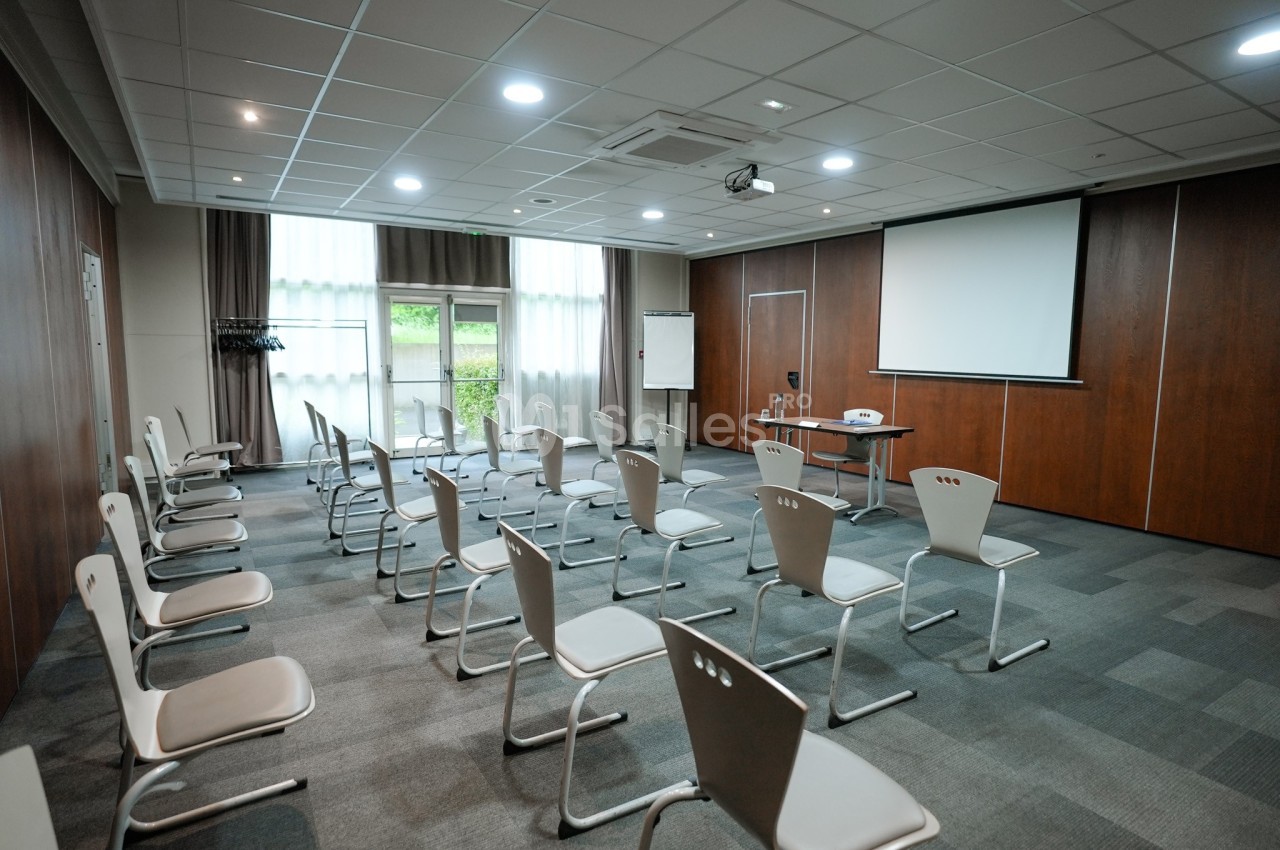 Salle de réunion lumineuse avec des chaises alignées, un projecteur, un écran et un tableau blanc.