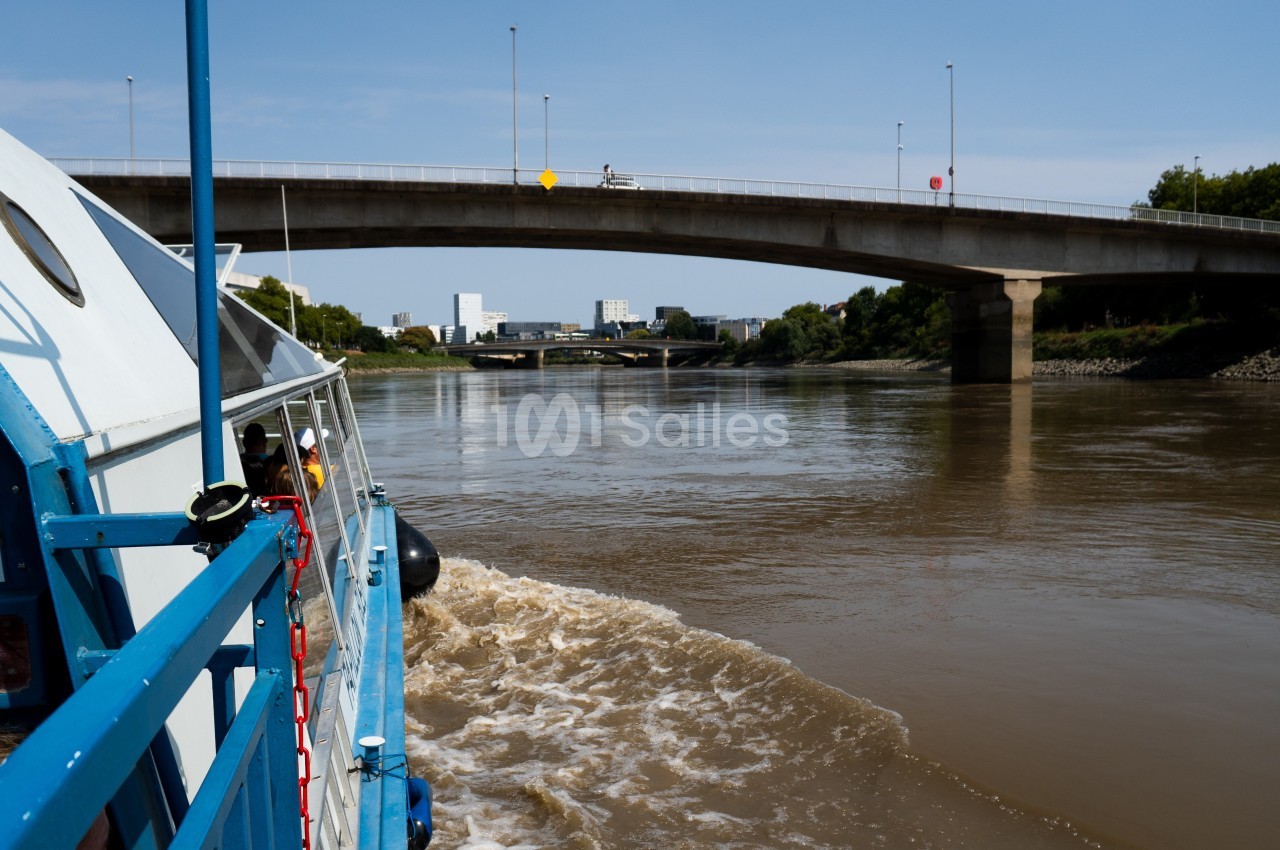 Vue depuis un bateau naviguant sur une rivière, avec un pont en béton et des bâtiments en arrière-plan.