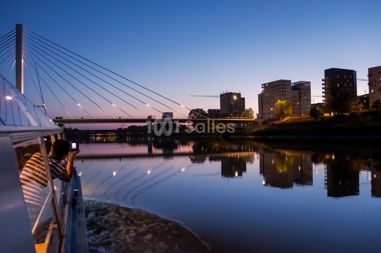 Vue d'un pont moderne et de bâtiments au bord d'une rivière au crépuscule, capturée depuis un bateau.