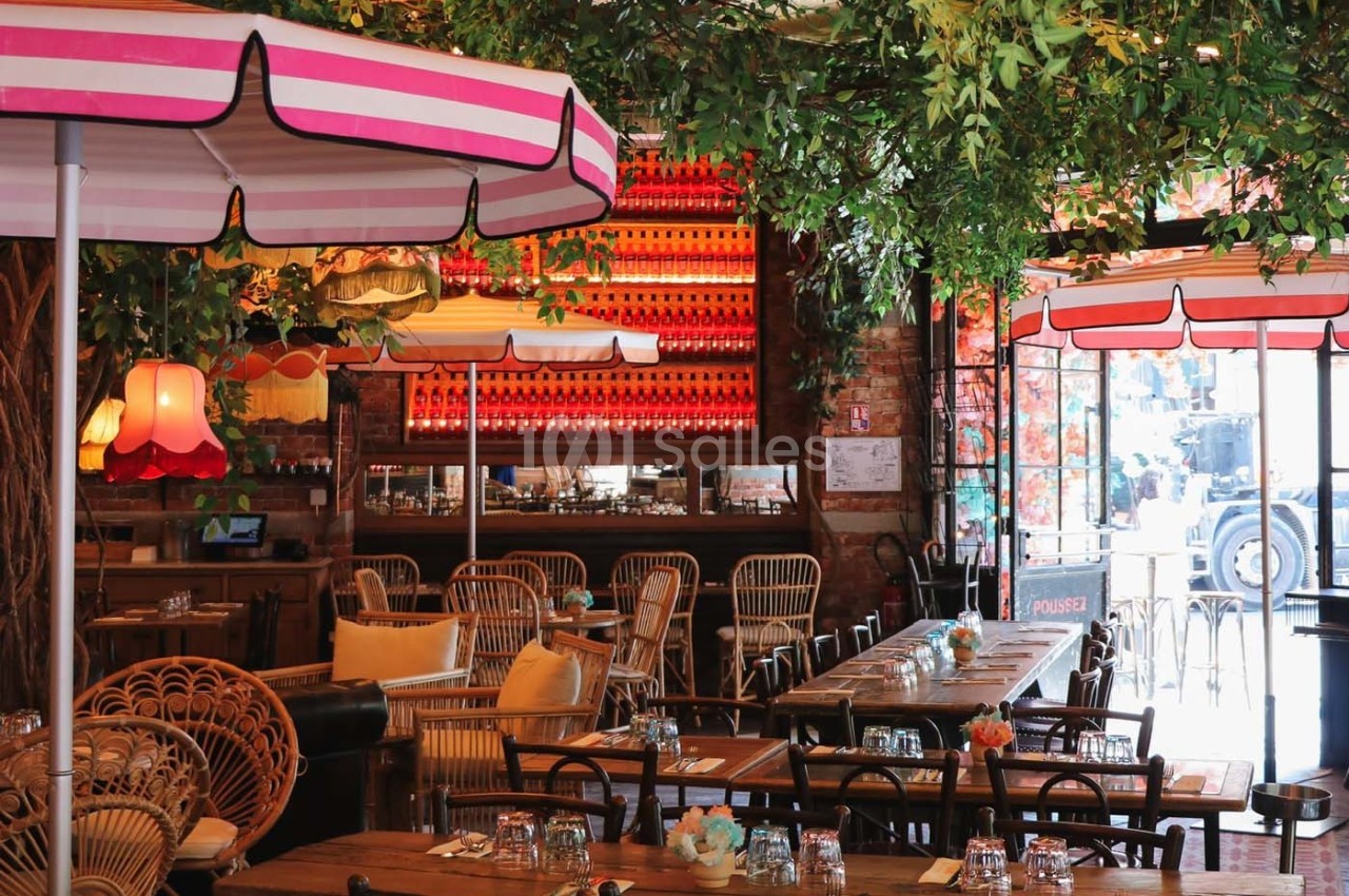Salle de restaurant décorée avec des parasols colorés, des plantes suspendues et des tables en bois dressées.